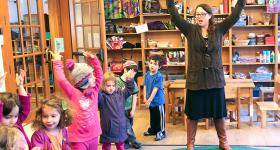 teacher raises arms high to show preschoolers in her class how to stretch upward