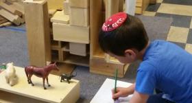 Small boy writes with toy animals in front of him.