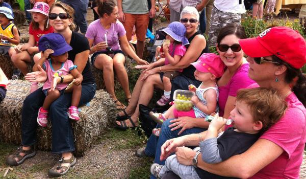 Large group of women sit on hay bales holding young preschool children on their laps