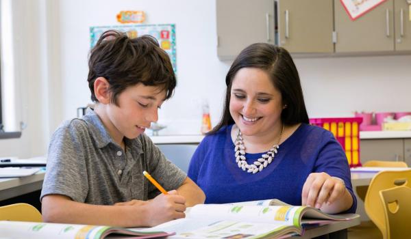 Teacher sits with student at a table.