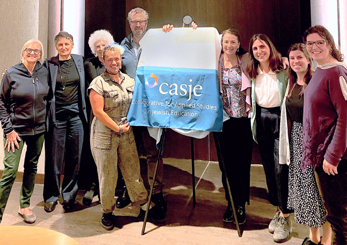 Advisory Board members stand in front of an easel. There's a cloth covering the sign that reads CASJE: Collaborative for Applied Studies in Jewish Education