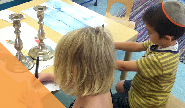 two young students working at desk in classroom; candlesticks on desk