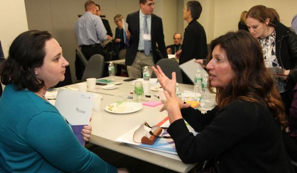 Group of CASJE affiliated professionals talk in small groups after meeting ends; one holds CASJE folder in arm