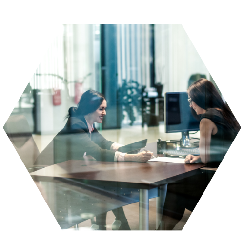 Two people sitting at a desk behind a glass door (image is hexagon shaped)