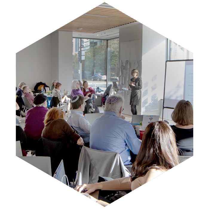 group of professionals at large CASJE convening, one person presenting in front (image is hexagon shaped)