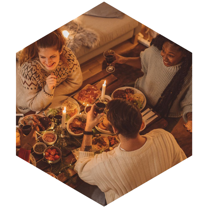 Three people at a dinner table, two candles and food on the table (image is hexagon shaped)