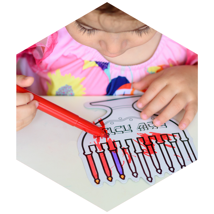 pre-school child colors in coloring sheet with menorah (image is hexagon shaped)