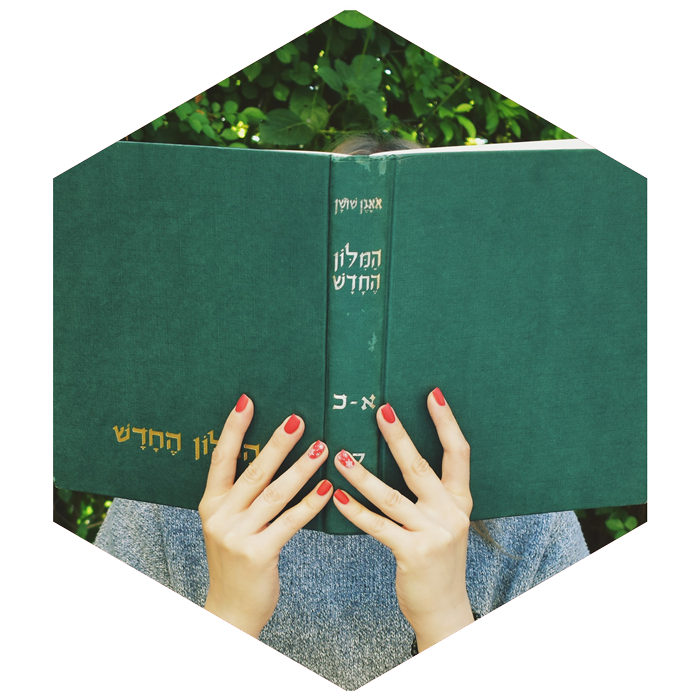 girl holding Hebrew book with green cover open in front of her face (image is hexagon shaped)