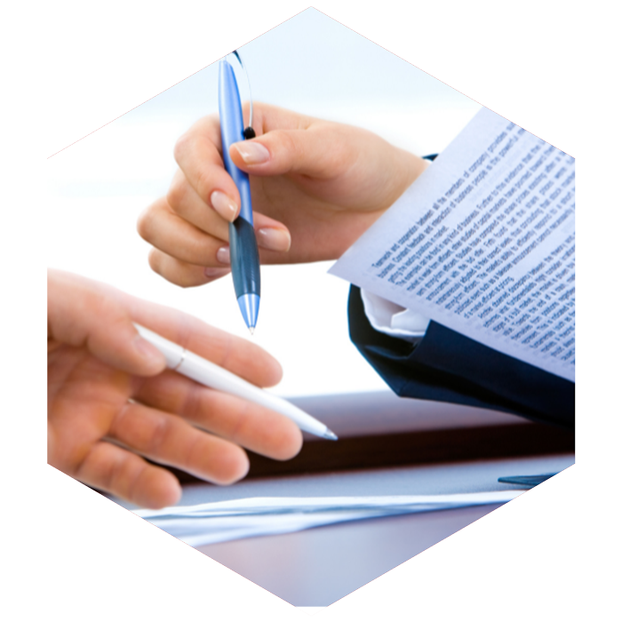 two people holding pens in their hands review documents (image is hexagon shaped)