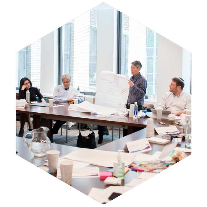 Group of CASJE affiliatesw around a conference table, one stands holding a large white sheet of paper for the group to see (image is hexagon shaped)