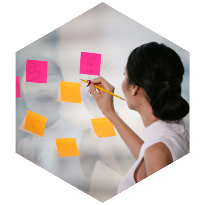 professional female writes on sticky notes posted on clear window (image is hexagon shaped)