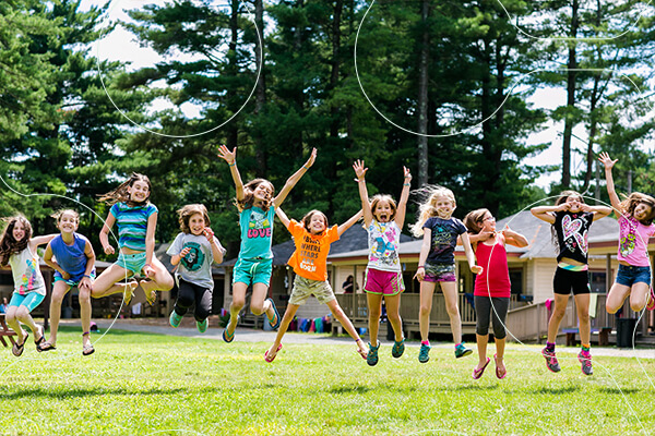 group of students jump excitedly outside at a summer camp