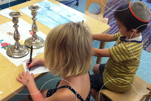 two young students working at desk in classroom; candlesticks on desk