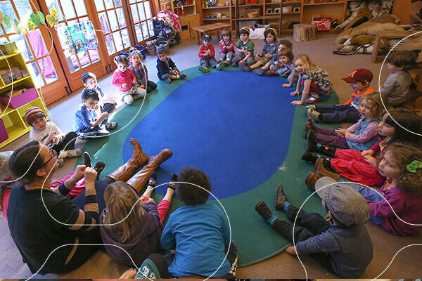 preschool students sit around round blue rug in classroom