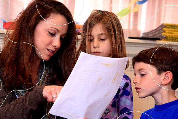 teacher holds sheet of paper while two young students look at it with her