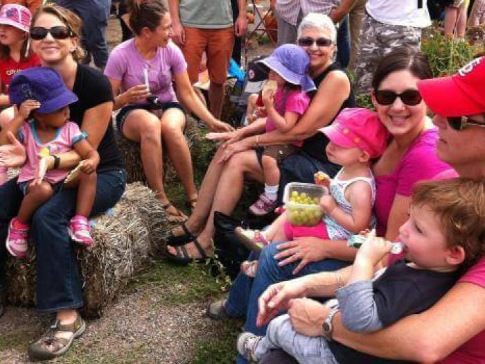 Large group of women sit on hay bales holding young preschool children on their laps