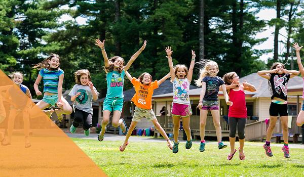 group of students jump excitedly outside at a summer camp