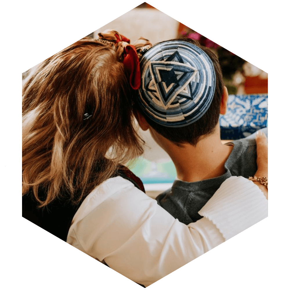 Back of woman and young boy wearing a kippah with heads together (image is hexagon shaped)