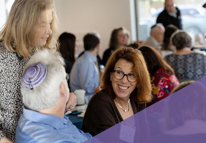 group of professionals at CASJE event: one female stands behind seated male with back to camera, another female laughs