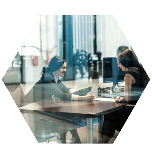 Two people sitting at a desk behind a glass door (image is hexagon shaped)
