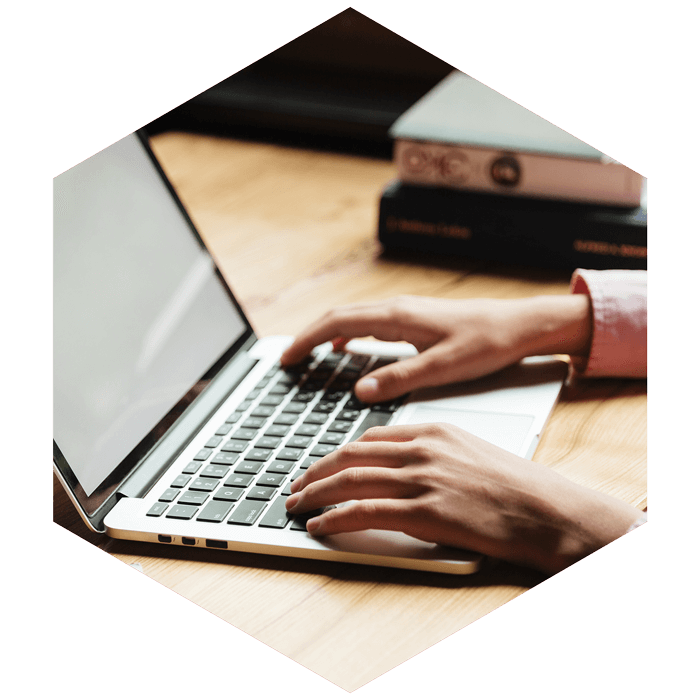 male hands typing on a laptop (image is hexagon shaped)