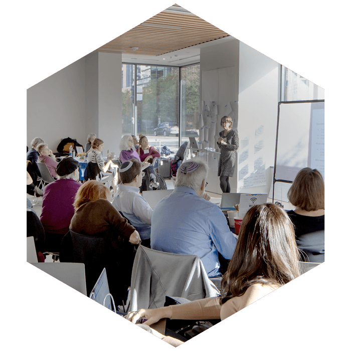 group of professionals at large CASJE convening, one person presenting in front (image is hexagon shaped)