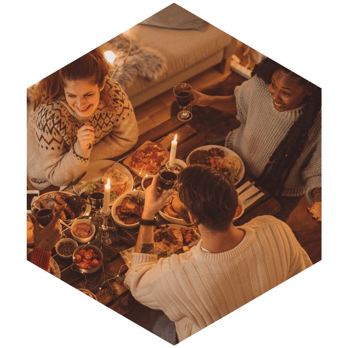 Three people at a dinner table, two candles and food on the table (image is hexagon shaped)