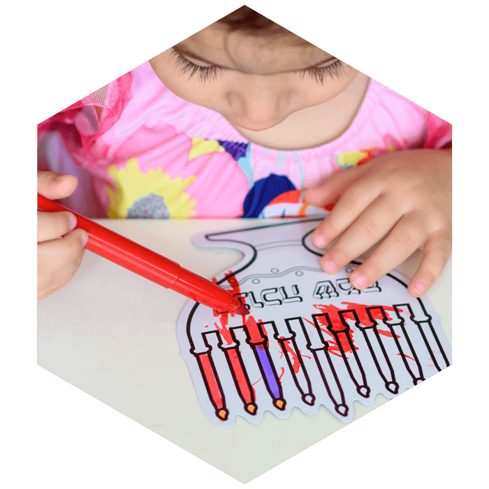 pre-school child colors in coloring sheet with menorah (image is hexagon shaped)