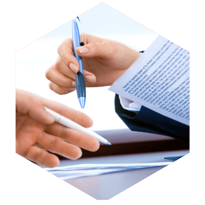two people holding pens in their hands review documents (image is hexagon shaped)