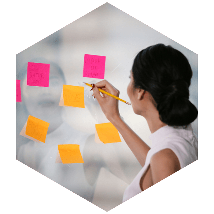 professional female writes on sticky notes posted on clear window (image is hexagon shaped)