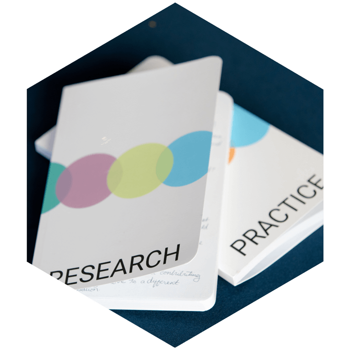 Two notebooks, one says Research the other, Practice (image is hexagon shaped)