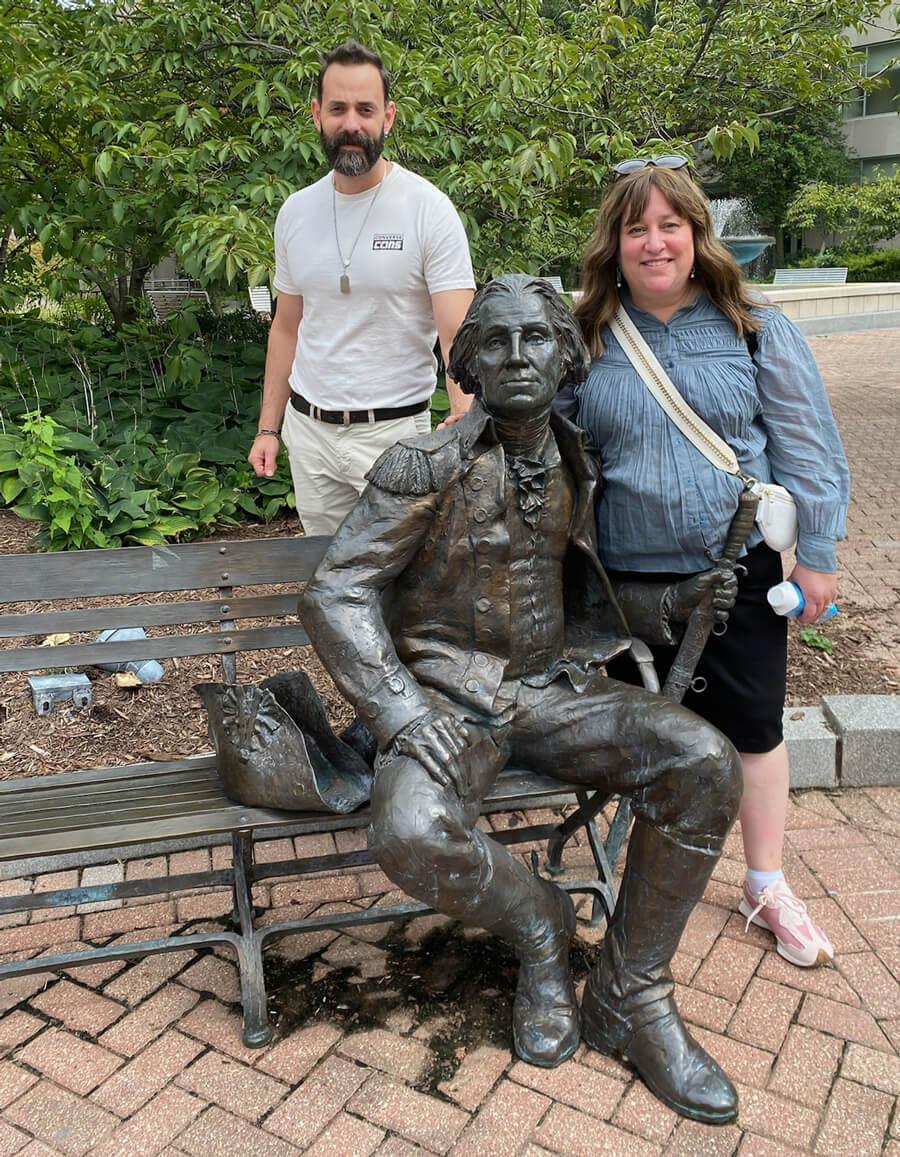Two CASJE fellows stand beside a statue of George Washington on a bench in the GW Student Plaza